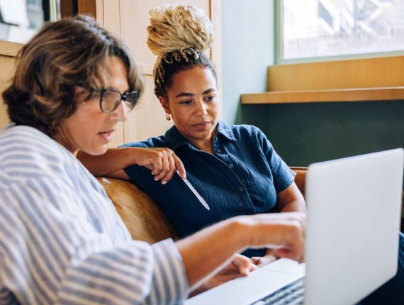 Two businesswomen sitting indoors looking at a laptop